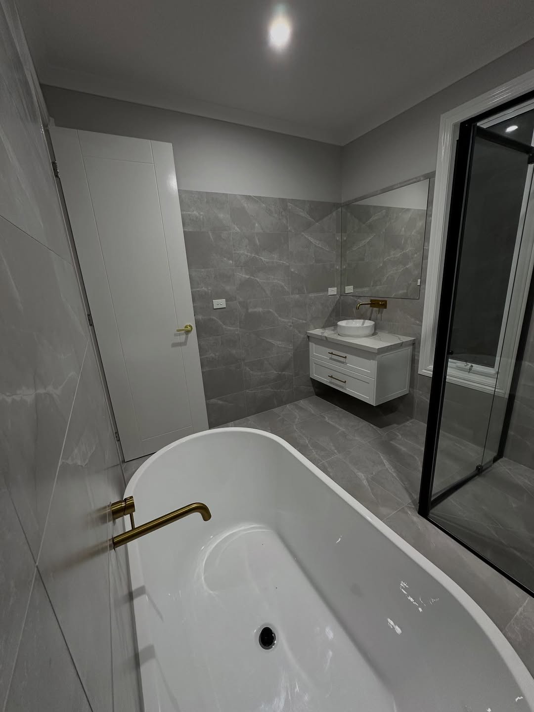 Grey tiled bathroom with freestanding bath and gold tapware
